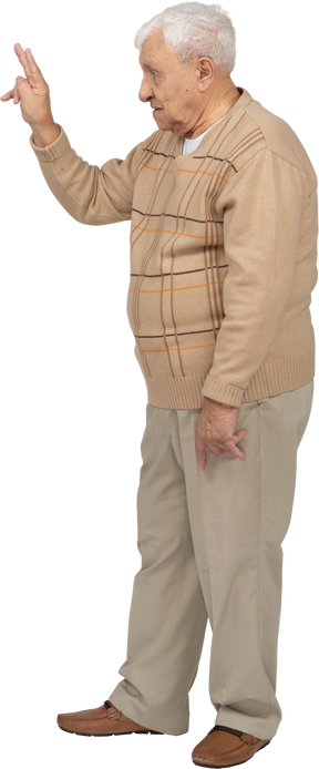 Vista lateral de un anciano con ropa informal que muestra el signo v