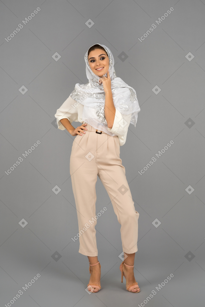 Confident cheerful young woman in white headscarf touching her face and looking aside