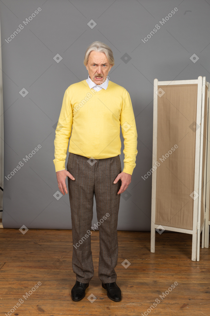 Vista frontal de un malvado anciano tejiendo las cejas mientras mira a la cámara