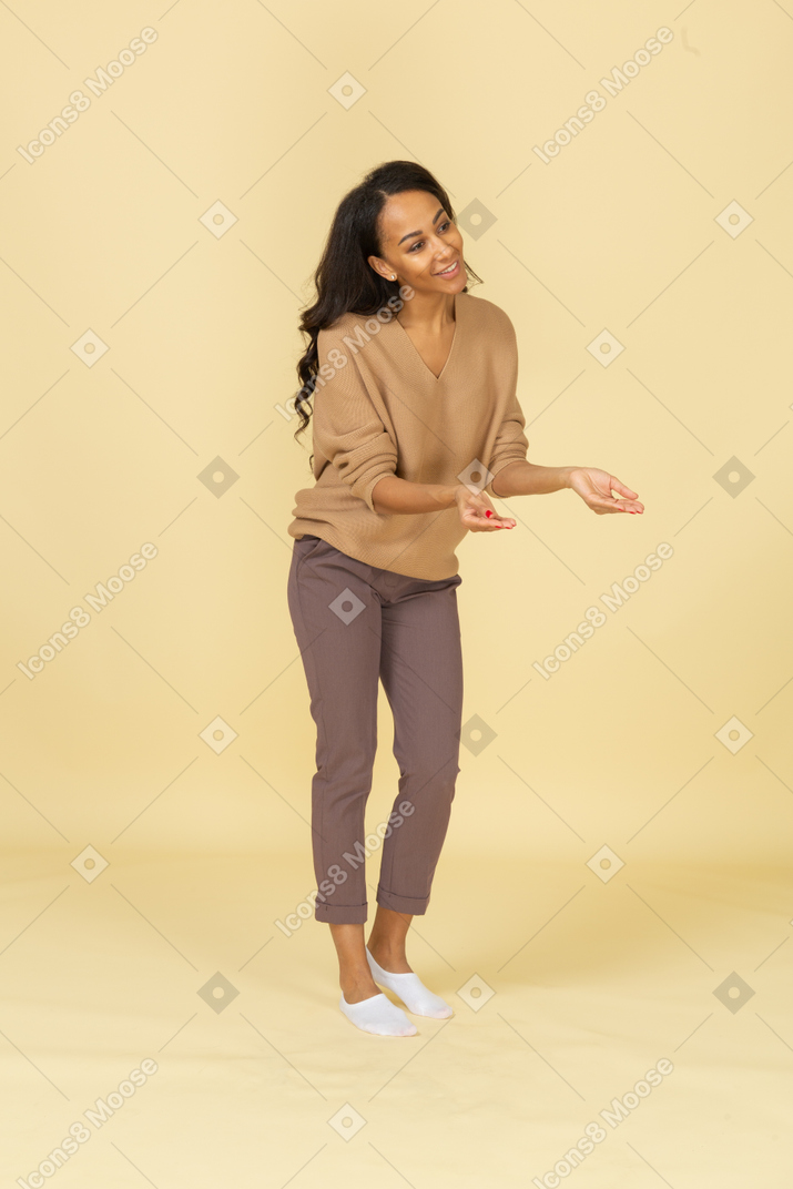 Three-quarter view of a dark-skinned smiling young female outstretching her hands