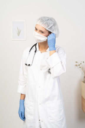 Vista frontal de uma jovem médica tirando a máscara