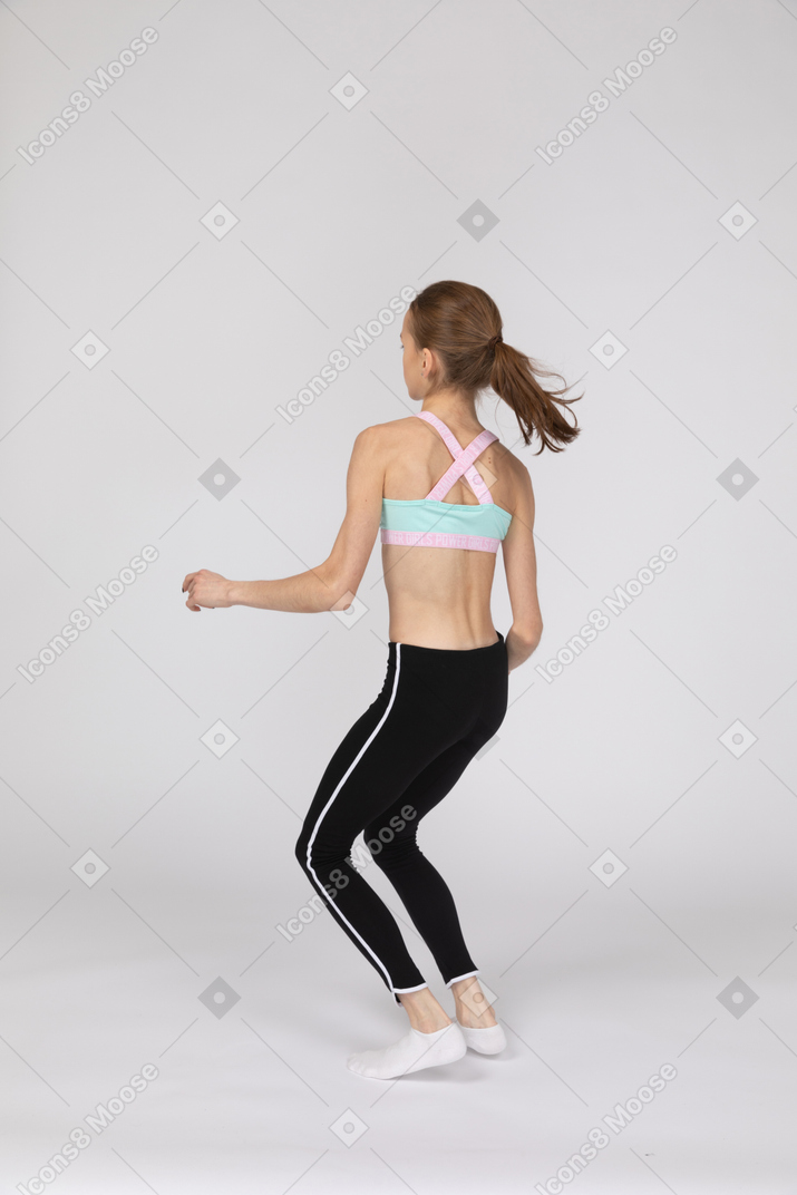 Vista traseira de três quartos de uma adolescente em roupas esportivas agachada enquanto dança