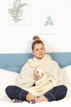 Front view of an ill young lady wrapped in white blanket staying in bed