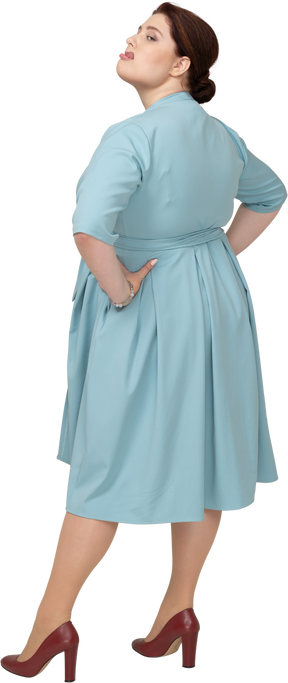 Вид сбоку женщины в синем платье позирует с руками на бедрах