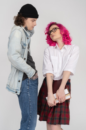 Um adolescente confuso e uma jovem de cabelo rosa usando óculos, olhando um para o outro