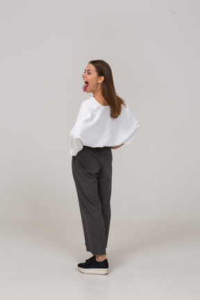 Vista posteriore di tre quarti di una giovane donna urlante in abiti da ufficio che mostra la lingua
