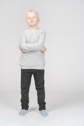 Front view of a thoughtful kid boy raising head and crossing hands