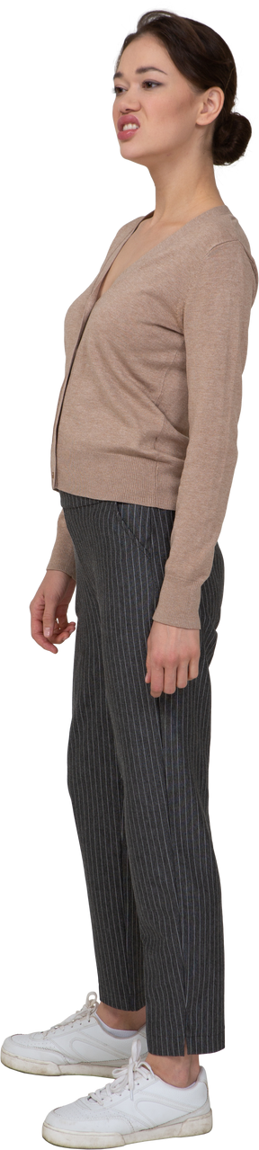 Vista de tres cuartos de una dama haciendo muecas en suéter y pantalones mirando a un lado
