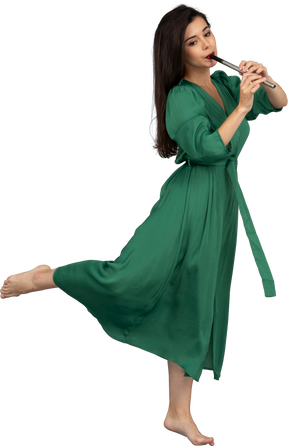 Side view of a barefooted young lady in green dress playing the flute
