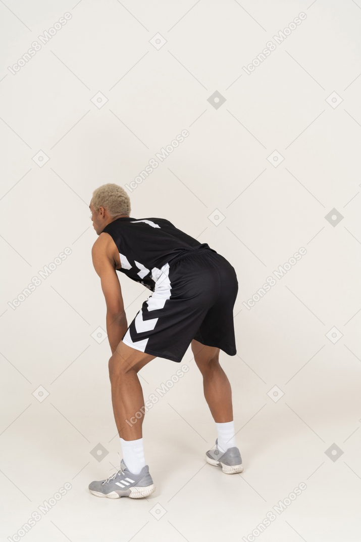 Three-quarter back view of a young male basketball player waiting for something