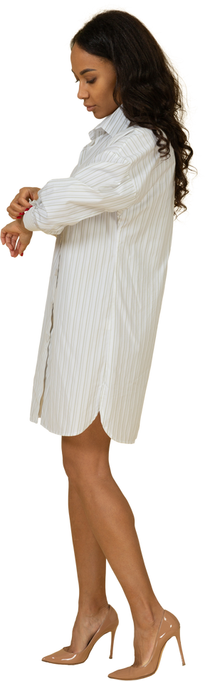 Vista lateral de uma jovem mulher de pele escura em um vestido branco abotoando a manga
