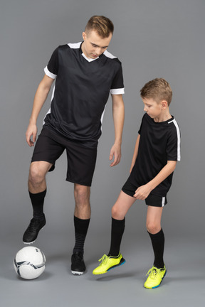 De cuerpo entero de un joven entrenando a un niño pequeño cómo jugar fooyball