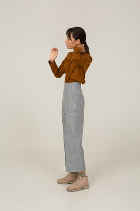 Side view of a young asian female in breeches and blouse touching neck