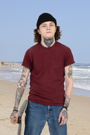 A man standing on a beach holding a skateboard