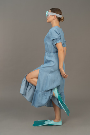 シュノーケリングマスクと足ひれで片足で立っている若い女性の側面図