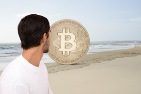 A man looking at a bitcoin on the beach
