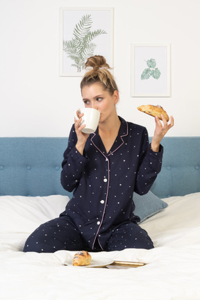 Vue de face d'une jeune femme en pyjama prenant son petit déjeuner au lit