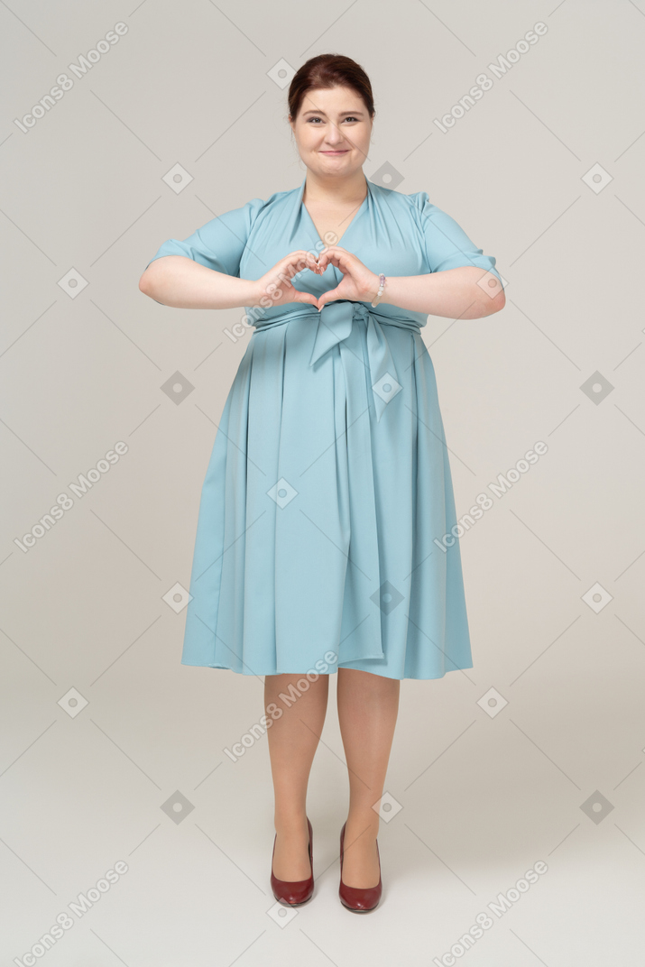 Vista frontal de uma mulher de vestido azul mostrando um gesto de coração