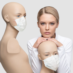 A woman standing next to a couple of mannequins in face masks 