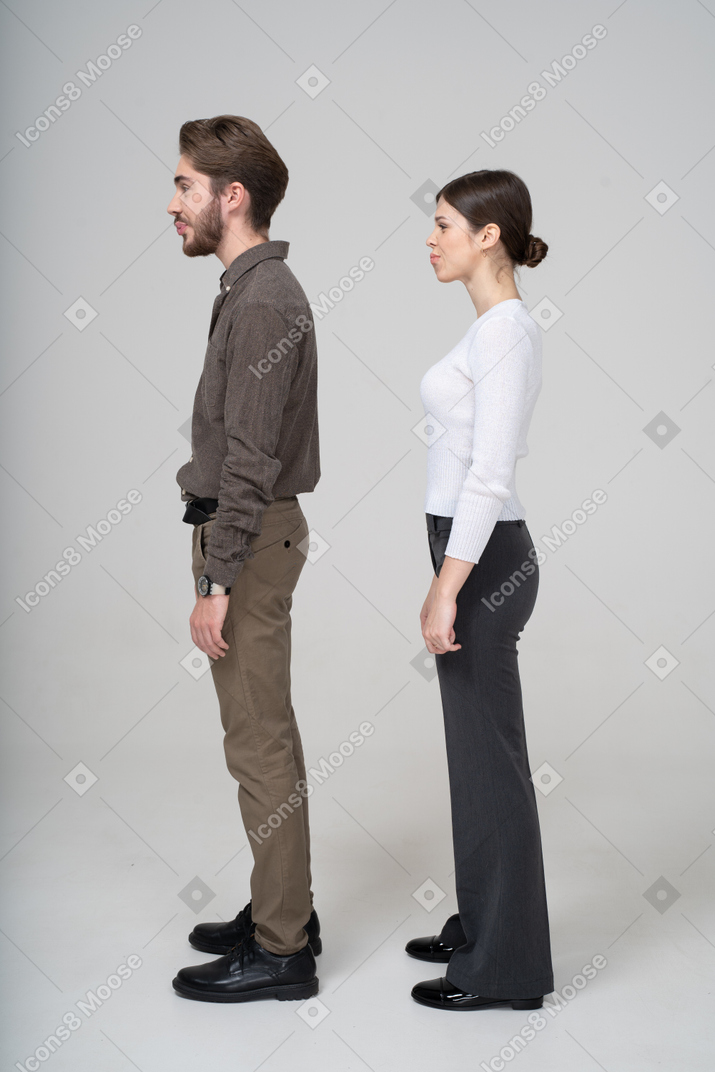 困惑的做鬼脸的年轻夫妇，在办公室服装中的侧视图