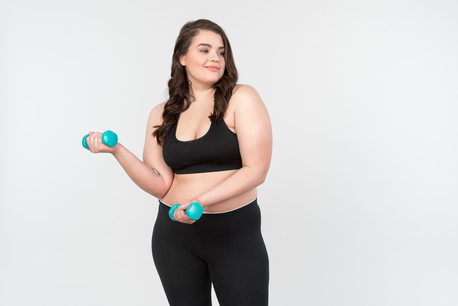Young plus-size model in sportswear holding hand weights
