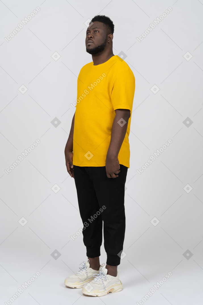 Dreiviertelansicht eines jungen dunkelhäutigen mannes in gelbem t-shirt, der still steht