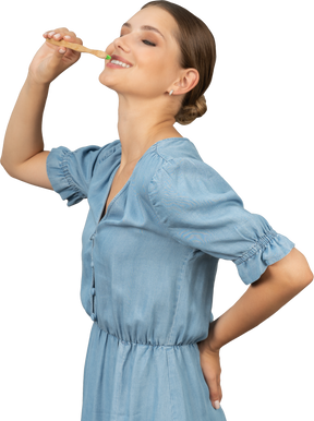 Three-quarter view of a young woman in blue dress brushing her teeth