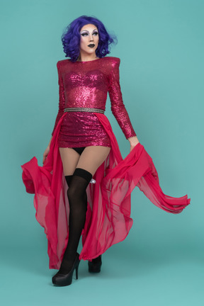 Vista frontal de una drag queen con un vestido de lentejuelas rosas que riza una falda larga mientras camina