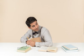 Estudiante adulto joven sentado en la mesa y escribiendo algo en el libro