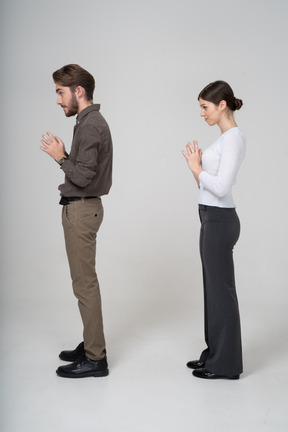 Side view of a sly young couple in office clothing holding hands together