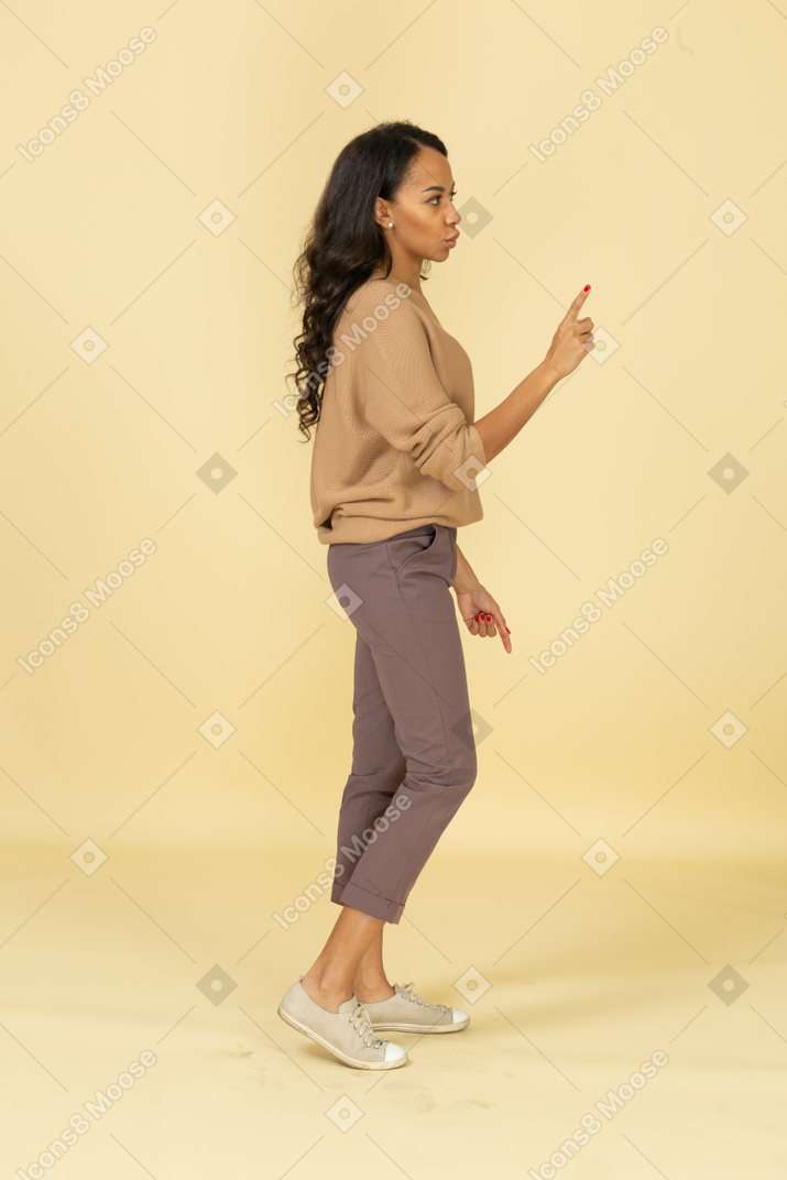 Side view of a cautious dark-skinned young female raising hand