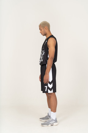 Vista lateral de un joven jugador de baloncesto masculino de pie y mirando hacia abajo