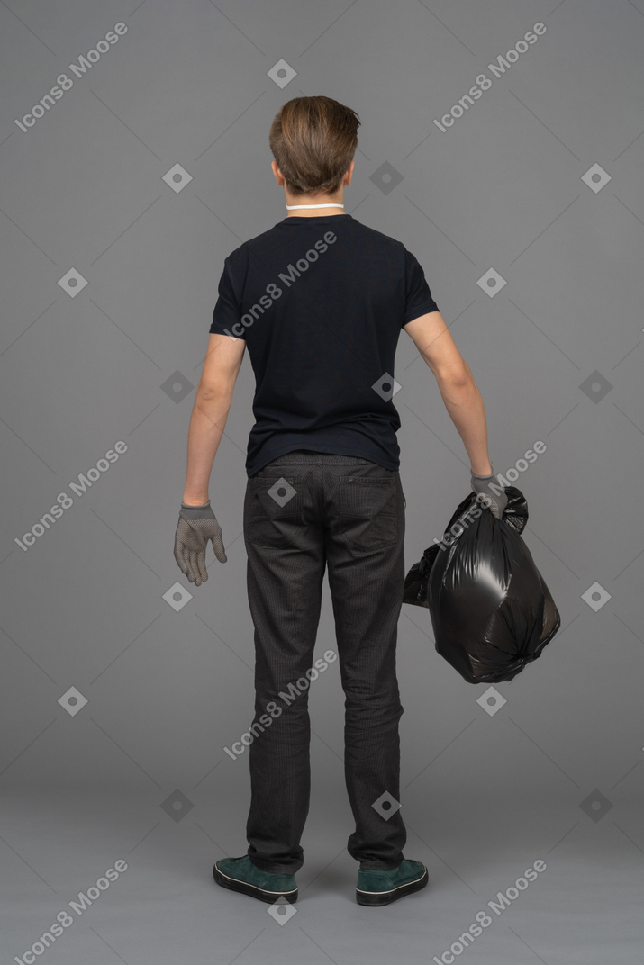 A man holding a black trash bag backwards to camera