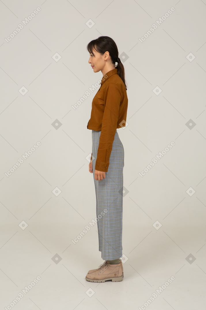 Vista laterale di una giovane donna asiatica in calzoni e camicetta in piedi ancora