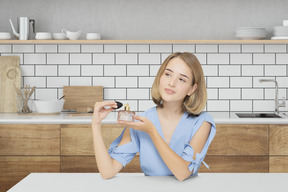 Jeune femme assise dans la cuisine et tenant une bouteille de parfum