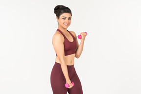 Young indian woman in sportswear lifting hand weights