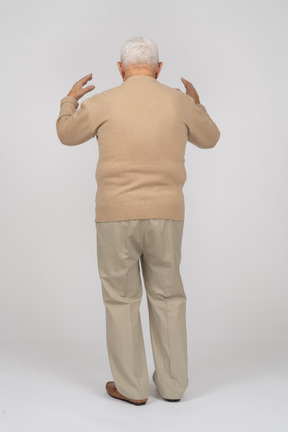 Rückansicht eines alten mannes in freizeitkleidung, der mit erhobenen händen steht