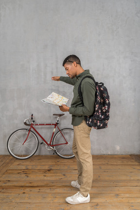 Side view of a man with a backpack looking at a map and pointing aside