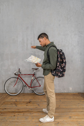 Vue latérale d'un homme avec un sac à dos regardant une carte et pointant de côté