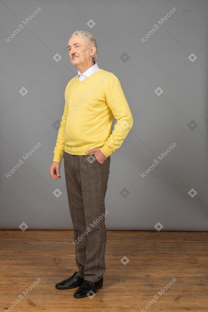 Three-quarter view of a displeased old man wearing yellow pullover and putting hand in pocket and looking aside