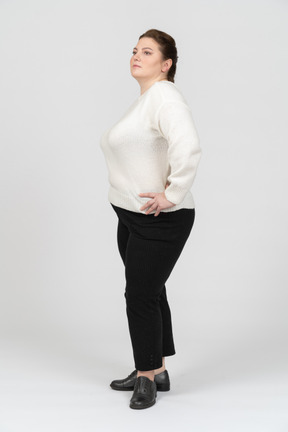 Plump woman in white sweater standing with hands behind head