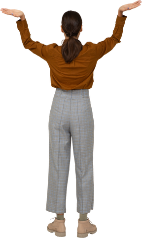 Vista posteriore di una giovane donna asiatica in calzoni e camicetta che alza le mani