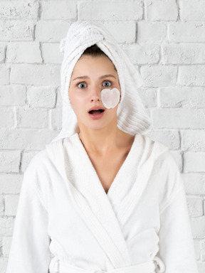 A shocked young woman in a robe with a cotton pad on her face