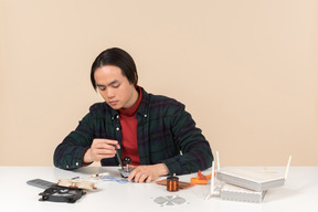 An asian geek guy in a dark checkered shirt, working with computer details