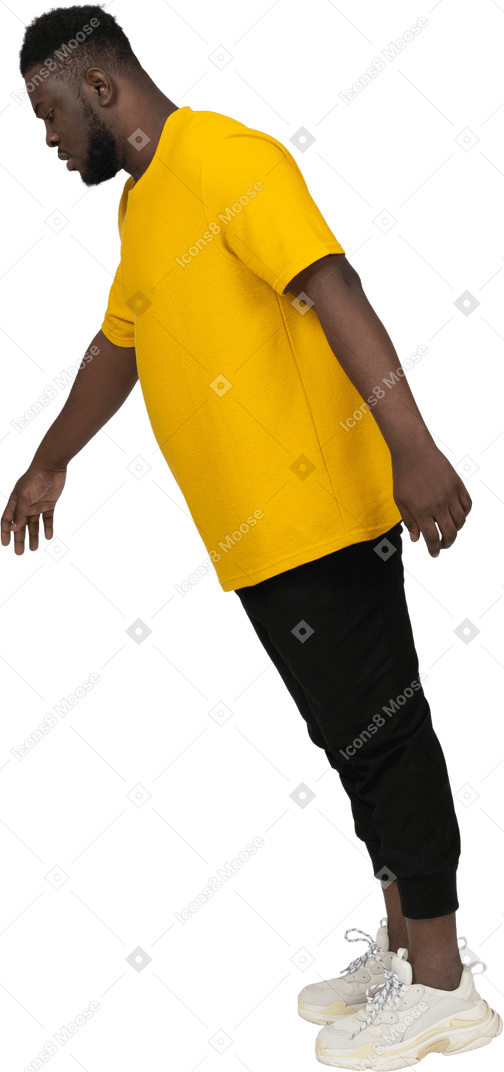 一个穿着黄色 t 恤的年轻深色皮肤男子低头跳跃的侧视图