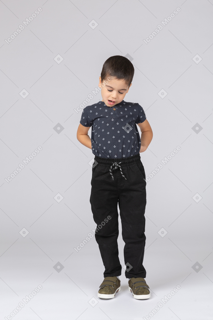 Front view of a cute boy posing with hands behind back and looking down