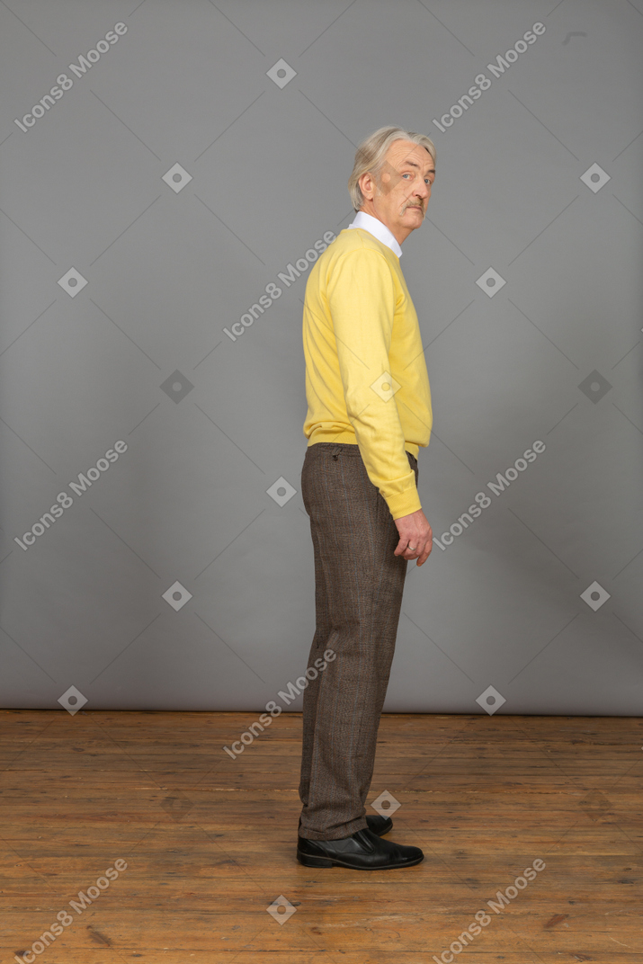Vue latérale d'un vieil homme curieux en pull jaune tournant la tête et regardant la caméra