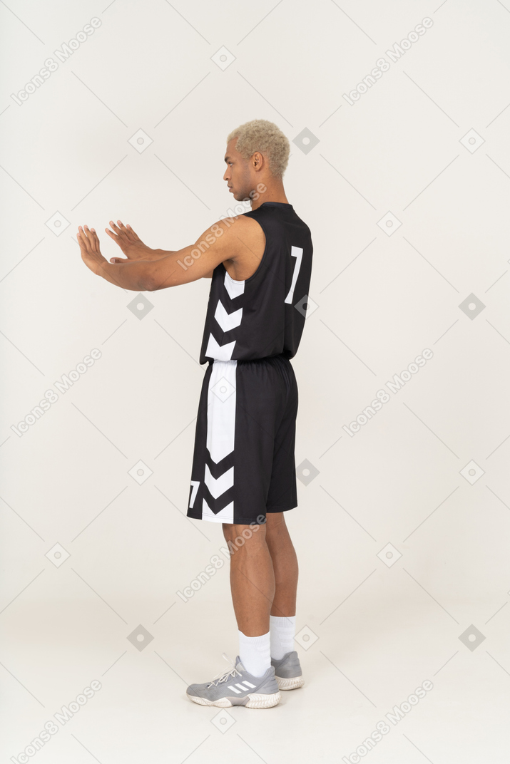 腕を伸ばして拒否する若い男性のバスケットボール選手の4分の3の背面図