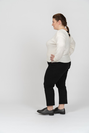 Женщина больших размеров в белом свитере стоит, положив руки на бедра