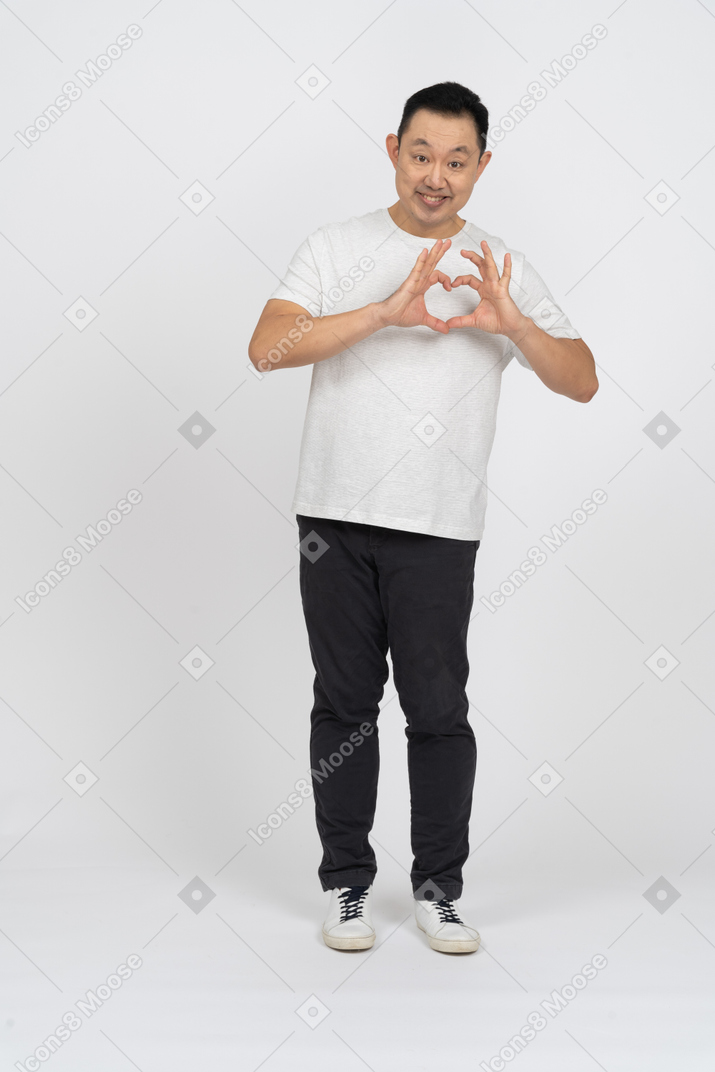 Front view of a happy man in casual clothes making heart with fingers and looking at camera